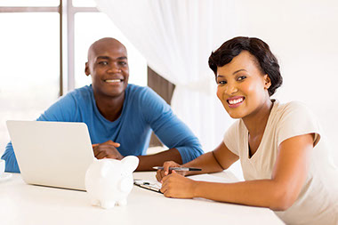 Image of young couple with laptop and piggy bank.