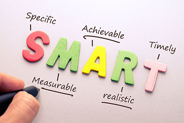 The word Smart spelled out with wood lettering and hand writing definition for setting a smart goal.