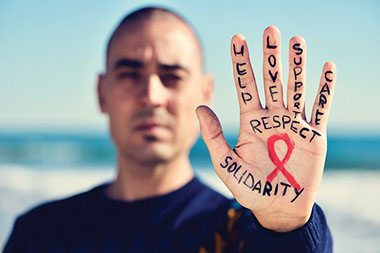 HIV and AIDS-how much do you know? Image of man's hold with the AIDS ribbon and words on fingers, that inlcude 'help', 'love', 'support', 'care.'
