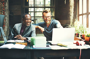 Two coworkers sitting at the table looking at the computer screen. Two coworkers sitting at the table looking at the computer screen.