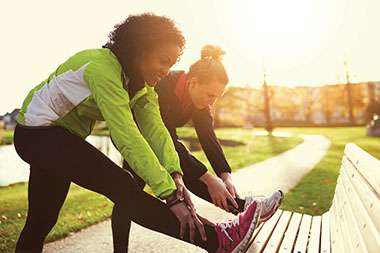 Two women stretching legs on bench.