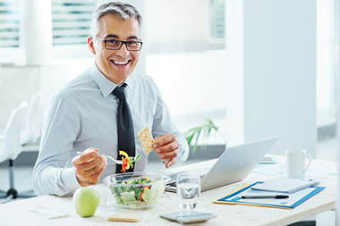 Image of business man eating a salad and cracker at his desk.