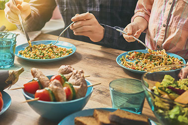 Close up on dinner table with food and hands with silverware about to eat.