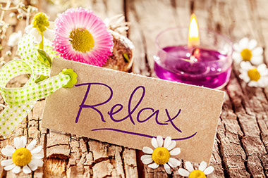 Image of relax sign decorated with various flowers and candle.