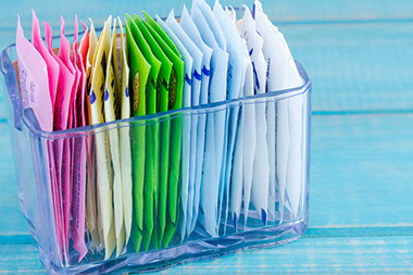 Packets of artificial sweeteners in glass container.