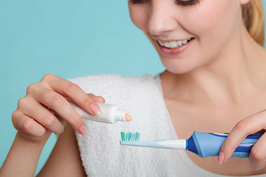 Image of women placing tooth paste on tooth brush.