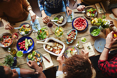Top view of food on the dinner table with people sitting around the table eating.
