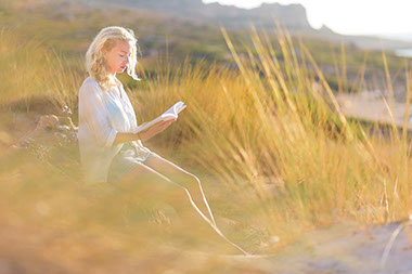 Image of women sitting in open field reading a book.