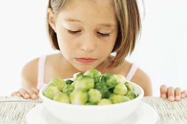 Image of young child with a sad face looking down at a bowl of brussel sprouts.