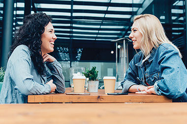 Two friends sitting at a cafe talking.