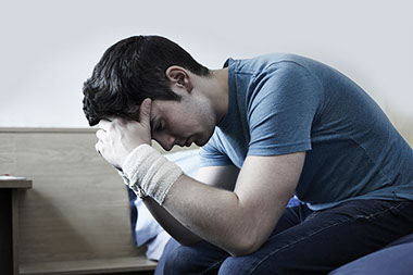 Man with head down and bandages around his wrists.