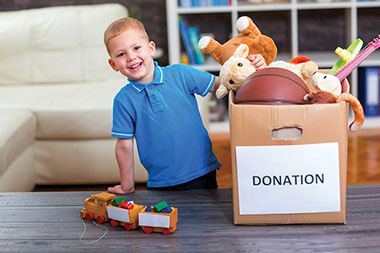 Getting kids to donate old toys. Image of happy child placing toys in donation box.