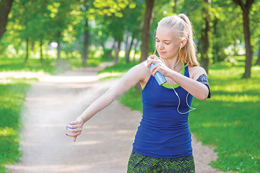 Banish biting bugs. Image of female spraying insect repellent on arm.