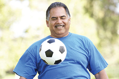 Best exercise for people with diabetes. Image of middle-aged Hispanic man playing with a soccer ball.