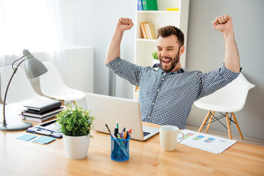 Happy man with arms up while setting at work desk.