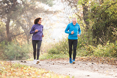 Senior couple running together outside in sunny autumn forest.