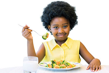 Young child smiling eating vegetables.