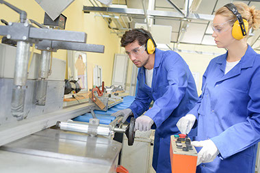 Image of workers wearing proper safety glasses and headphones while working on machinery.
