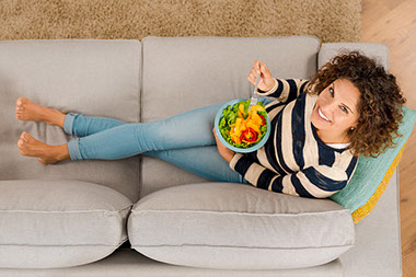 Top view of woman on the sofa eating a healthy salad.
