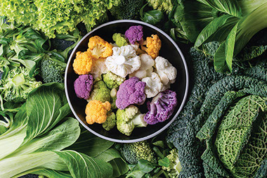Different colored cauliflower in bowl, surrounded by bok choy, cabbage, kale. Different colored cauliflower in bowl, surrounded by bok choy, cabbage, kale.