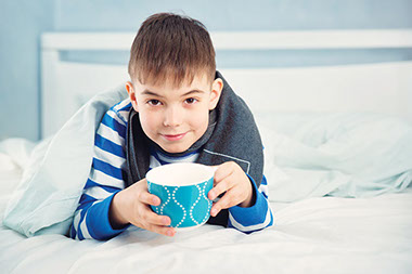 Image of child in bed holding a tea cup. Image of child in bed holding a tea cup.