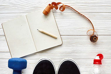 Fitness concept with notebook pencil for sport goals and resolutions, dumbbells and sneakers and water bottle.