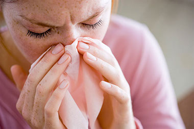 Image of person blowing nose with a tissue.