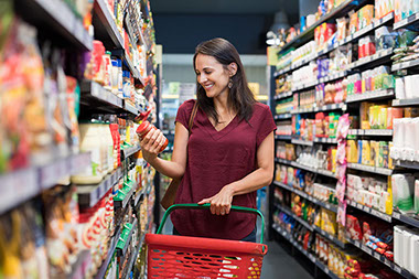 Smiling woman shopping in supermarket and reading food label.
