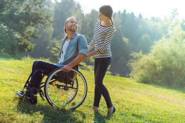 Women pushing man in wheelchair through the lawn.