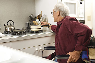 Image of eldery man in wheel chair cooking at his stove.
