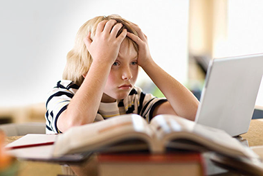 Image of stressed out boy sitting in front a a lapout with hands on head.