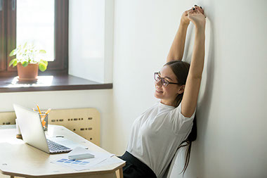 Female sitting at table with laptop, stretching arms up.
