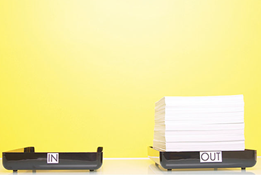 7 tricks to organize your office right now. Image of an empty 'In' tray and a full 'Out' tray.