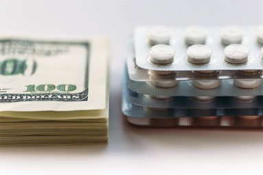 Small stack of money next to a small stack of pills.