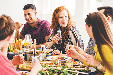 Group of friends sitting at table full of healthy snacks, salads and organic dishes.