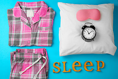 Image of sleeping mask, pillow, clock, and pajamas.