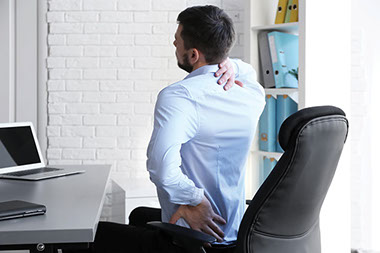 Man sitting on chair at desk stretching his back.