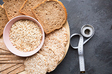 A bowl of oat flakes, wholegrain bread, crisps and tape-measure.