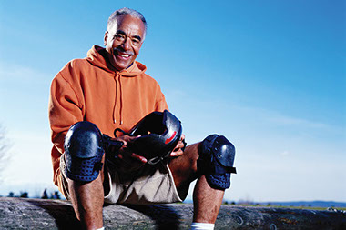 Image of older man wearing knee pads while holding a helmet.