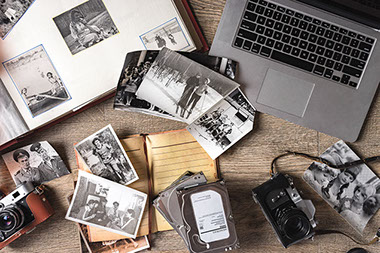 Old black and white photos on table next to camera, laptop, old photo album.